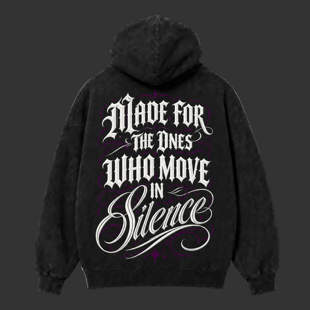 A black hooded sweatshirt shown from the back, featuring a large gothic-style graphic print in white and purple text that reads 'Made for the ones who move in silence' on a light gray background.
